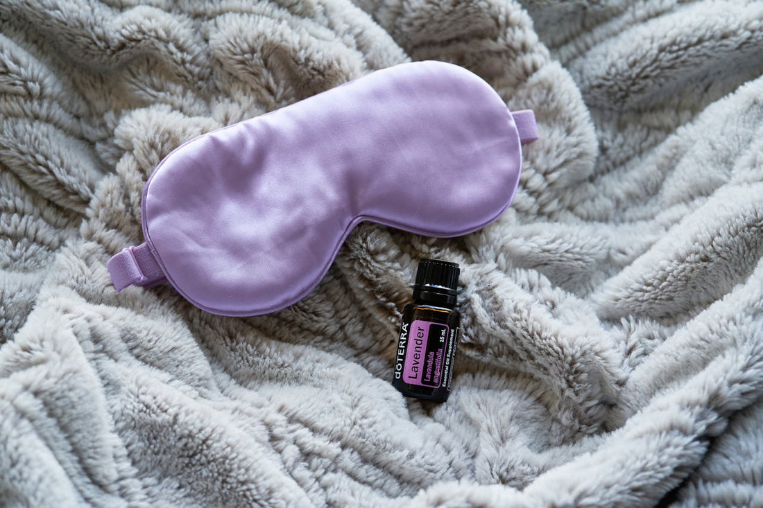 A lavender sleep mask and a bottle of essential oil on a blanket