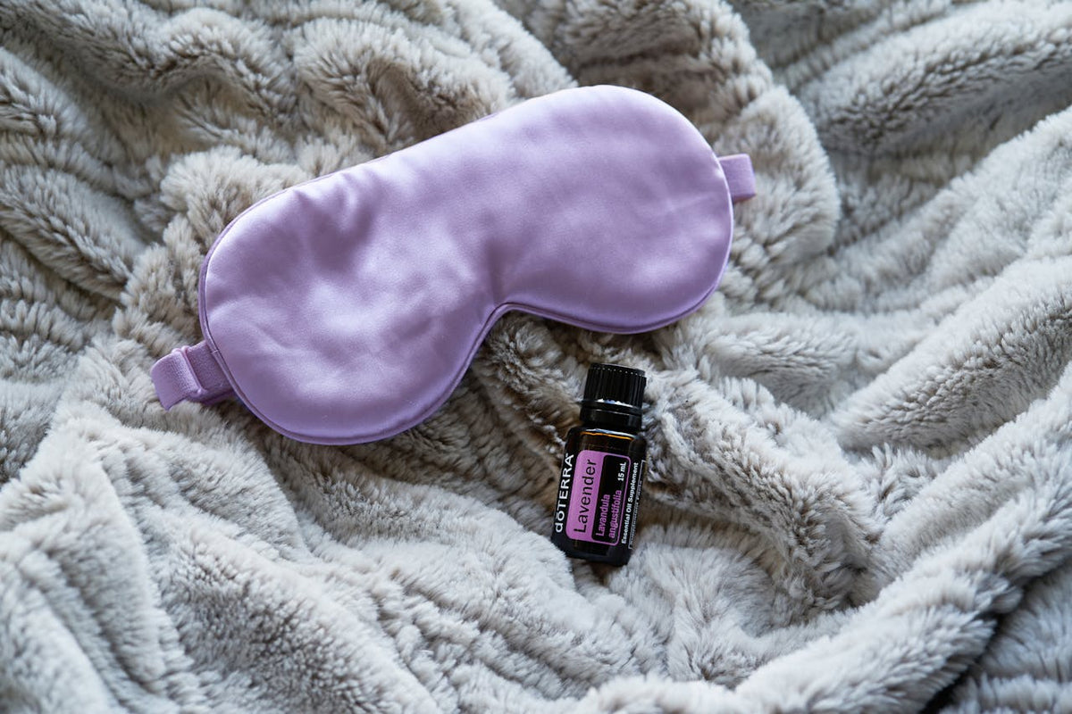 A lavender sleep mask and a bottle of essential oil on a blanket